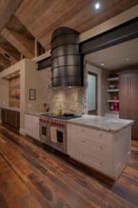 island blackened steel vent hood in rustic kitchen with vaulted ceiling and wolf range