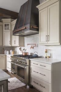 Custom Antique Vail Range Hood white backsplash cream cabinets stainless appliances copper accents