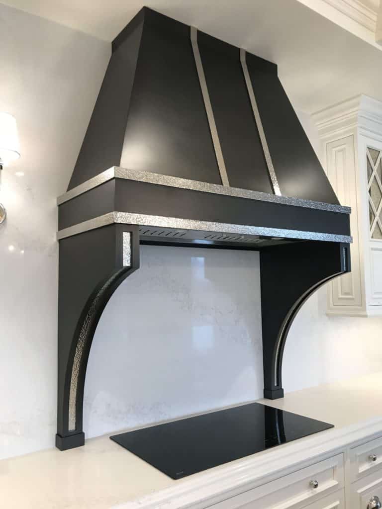 Black metal kitchen stove hood with hammered details in white kitchen