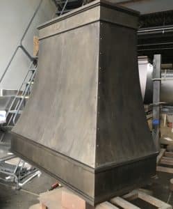 brown and gray washed tones on simple curved metal range hood with smooth rivets and channel seam on body