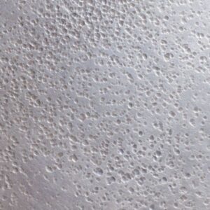 Close-up of Butterdish Pewter's white, textured surface features many small, uneven holes and bumps, resembling aerated or porous material like a sponge or textured plaster.