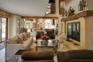 Highly decorated luxurious living room filled with couches, tables, fireplace, and rugs with the kitchen in the background