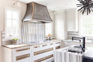 Dove creek metal range hood above an electric stove surrounded by white cabinets and modern fixtures