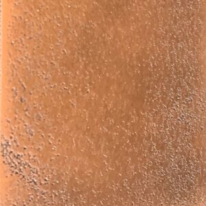 Close-up of the Copper Cast Sample shows a brown, textured surface with scattered gray specks and a slightly rough look. Lighting highlights subtle variations in its color and texture.