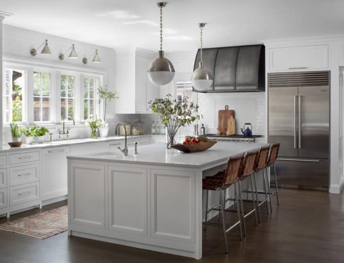 metal range hood in a fully furnished and designed kitchen with white cabinets, island table, and plants by the window