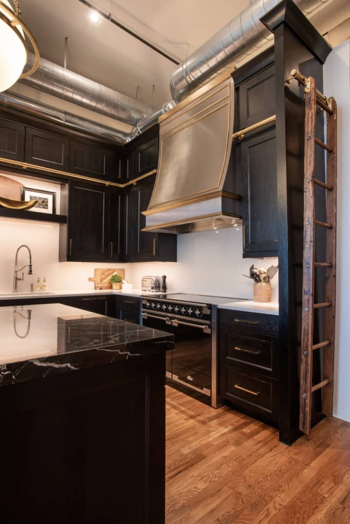 Example of a stainless and brass custom metal range hood used in an industrial space with high ceilings and dark wood cabinets with range hood by Raw Urth Designs.