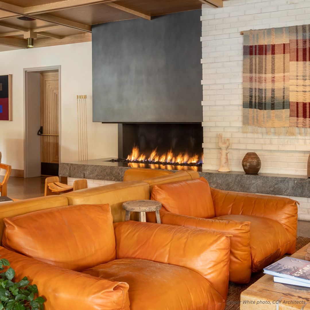 Cladding Gallery 2 A cozy living room features large orange leather armchairs before a modern Cladding Gallery 2 fireplace embedded in a brick wall. A woven tapestry adorns the wall, complemented by a small wooden stool and decorative pottery.
