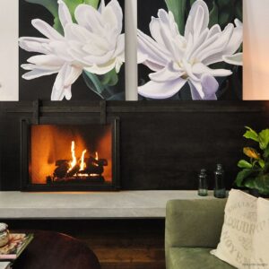 A modern living room features DoorsScreen 4 beneath two large white flower paintings, a green sofa with a printed cushion, and glass decor accents on a gray bench.