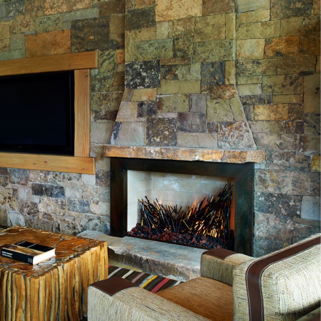 Fireplace GALLERY The Fireplace GALLERY features a modern rectangular design against a textured stone wall. A log-style coffee table and striped armchair enhance the cozy atmosphere, while a mounted flat-screen TV adds entertainment to the space.