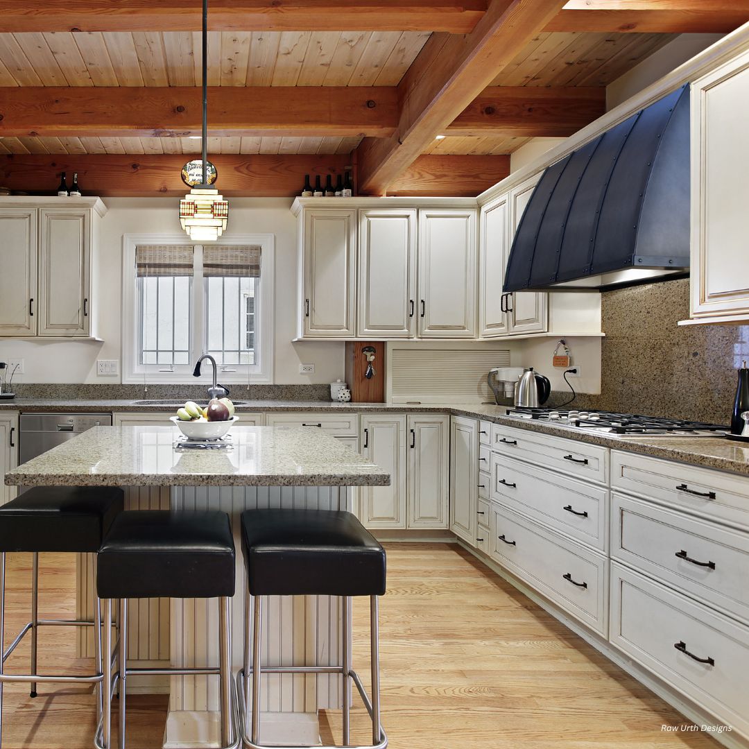 aspen-classic-gallery3 The aspen-classic-gallery3 kitchen features a spacious design with wooden beams, white cabinets, and granite countertops. It includes a large island with three black stools, a fruit bowl, modern stainless steel appliances like a range with a dark hood, wooden floors, and pendant lighting.