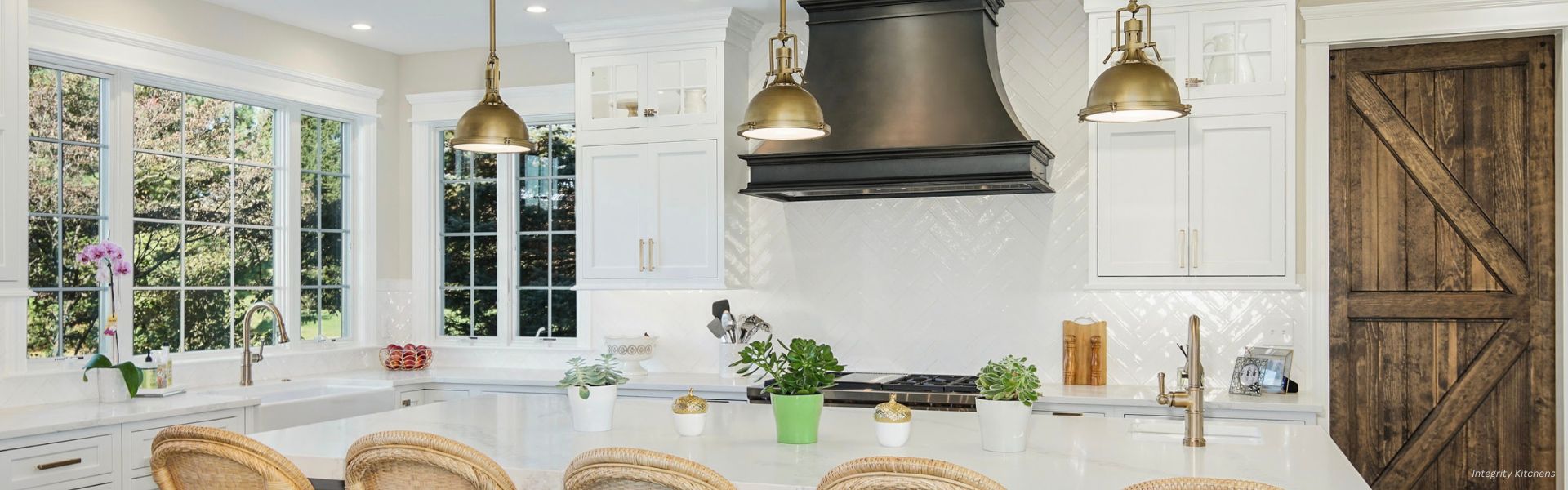 EVERGREEN-Montrose The EVERGREEN-Montrose features a bright, modern kitchen with large windows, white cabinets, a black range hood, gold pendant lights, a wood sliding barn door, wicker bar stools at a white island, and potted plants for decor.