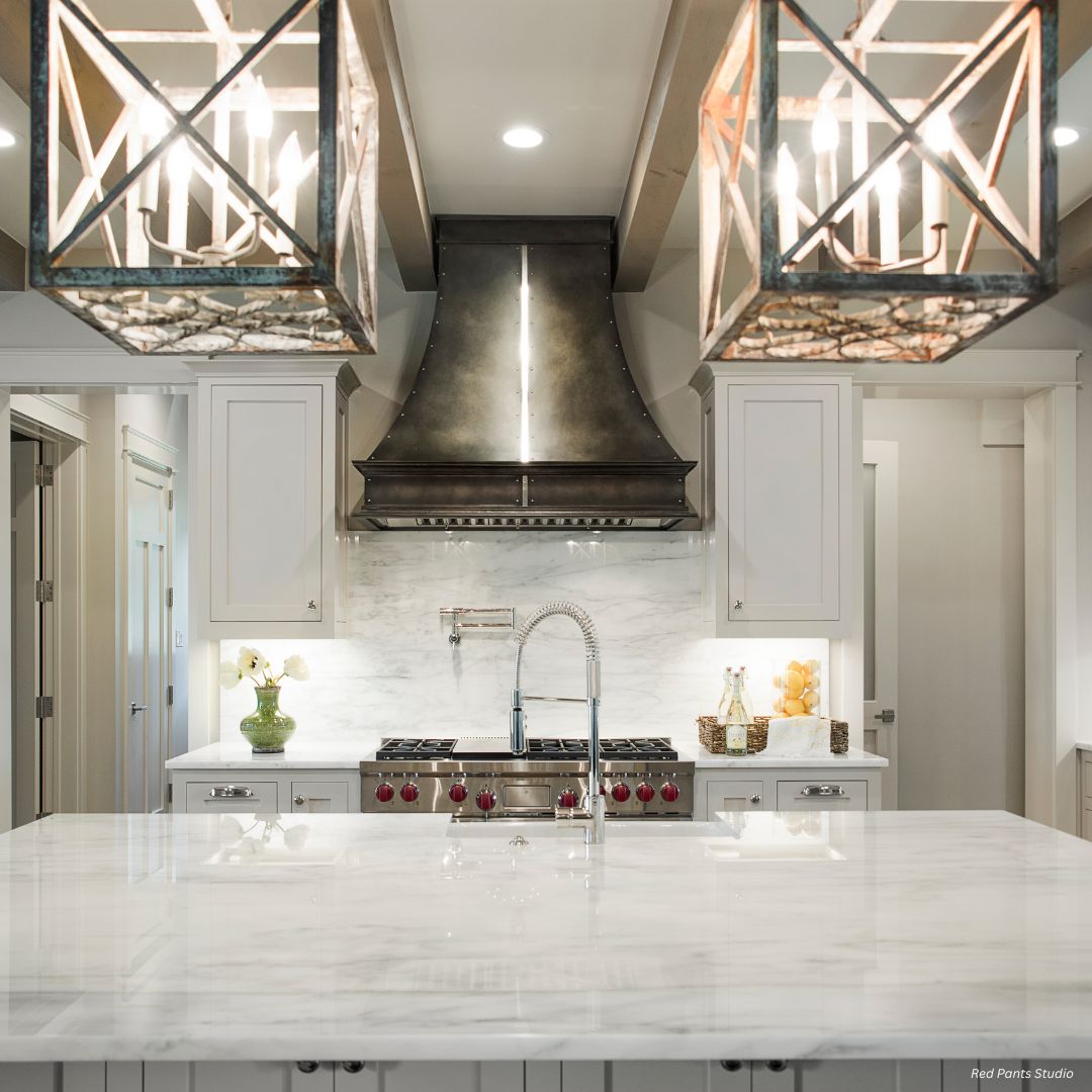 Montrose-tailored-gallery1√ A Montrose-tailored-gallery1√ kitchen features a marble island, stainless steel stove and range hood, white cabinetry, and two large geometric pendant lights above the island.