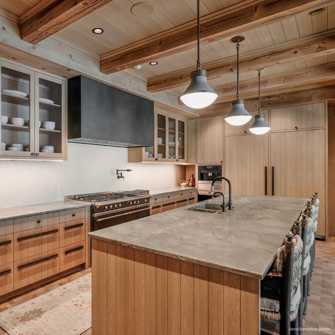 box-essential-gallery3√ The box-essential-gallery3√ features a modern rustic kitchen with wood cabinets, exposed beams, a spacious island with gray stone countertop, pendant lights, open shelving, built-in appliances, and warm neutral tones for an inviting feel.