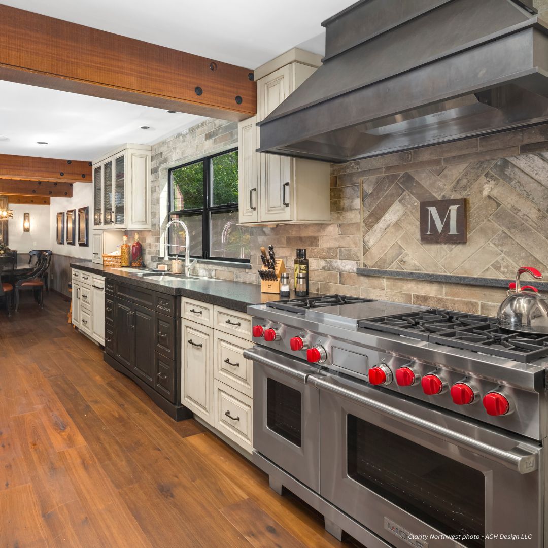 creed-essential-gallery1√ The creed-essential-gallery1√ kitchen features stainless steel appliances, double ovens, a six-burner stove with red knobs, dark countertops, black and white cabinets, wood floors, and a tiled backsplash with a framed letter "M".