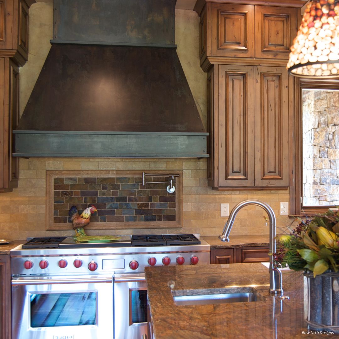 creed-tailored-gallery3√ A rustic kitchen showcases creed-tailored-gallery3√: a large metal range hood, wooden cabinets, tile backsplash, stainless stove with red knobs, farmhouse sink with gooseneck faucet, and a rooster figurine on the counter.