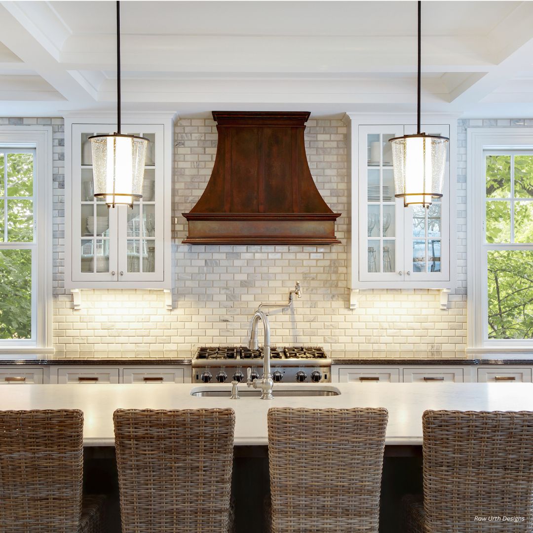 The montrose-refined-gallery3√ features a bright, modern kitchen with white cabinets, subway tile backsplash, a wood range hood, island sink, three wicker barstools, pendant lights overhead, and large windows for natural light.