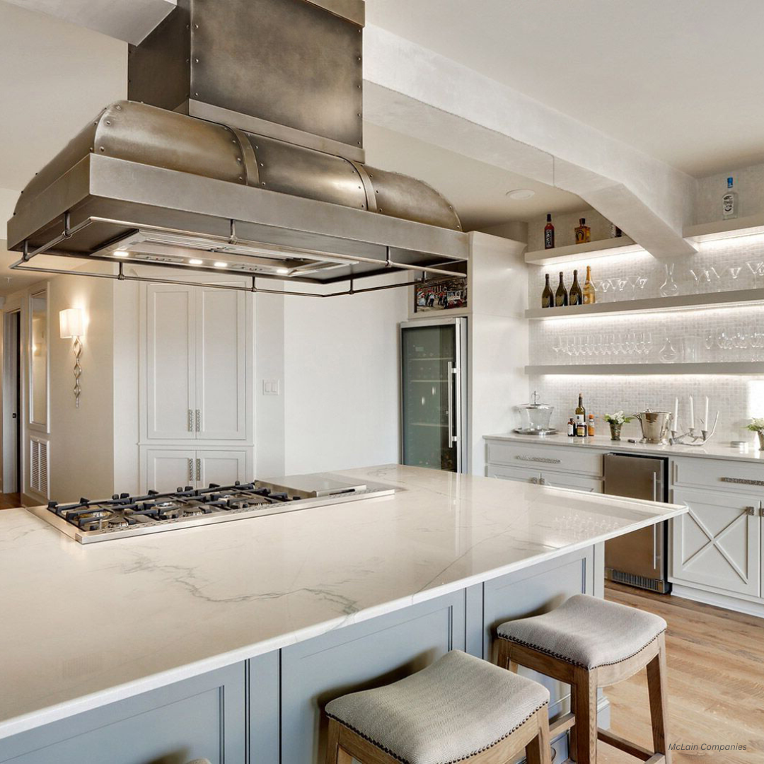 palisade gallery1 The palisade gallery1 features a modern kitchen with a spacious marble island, cushioned stools, stainless steel stove and range hood, built-in fridge, open shelving for glassware, and light wood floors in neutral tones.
