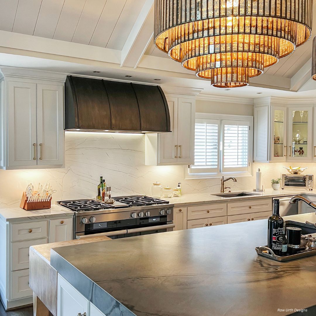 snowmass-classic-gallery1√ The snowmass-classic-gallery1√ kitchen features white cabinets, a spacious gray island, stainless steel appliances, a black range hood, and a decorative chandelier above the island with neatly arranged bottles and utensils on the counters.