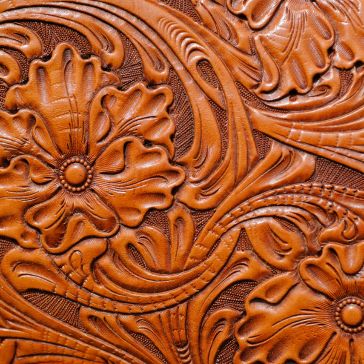 85 Product 85 features embossed brown leather with an intricate floral and leaf pattern, detailed swirling lines, and textured surfaces.