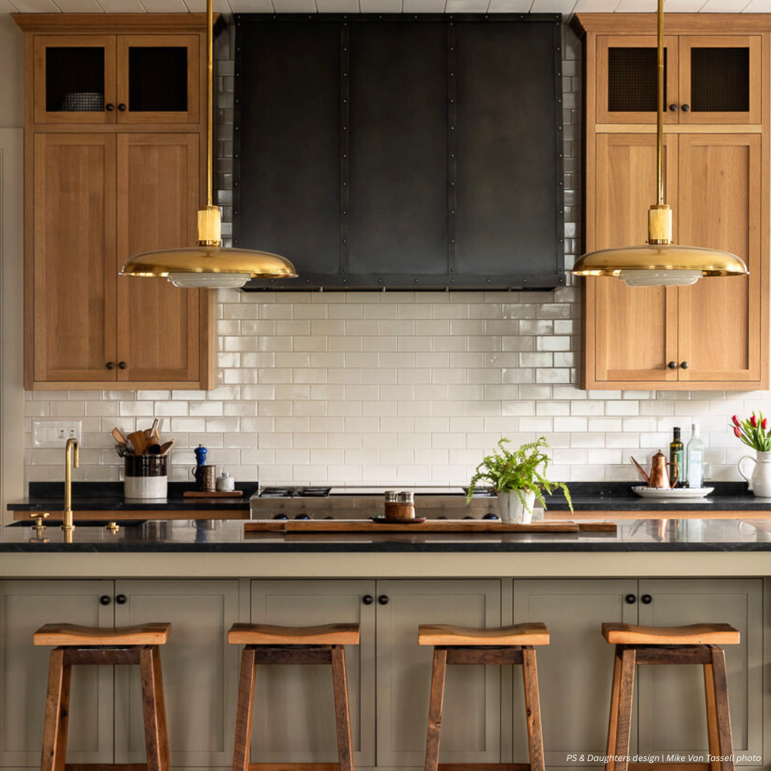 Aspen gallery1✅ Aspen gallery1✅ features a modern kitchen with light wood cabinets, a black metal range hood, white subway tile backsplash, dark countertops, three wooden stools, and brass pendant lights over the island.