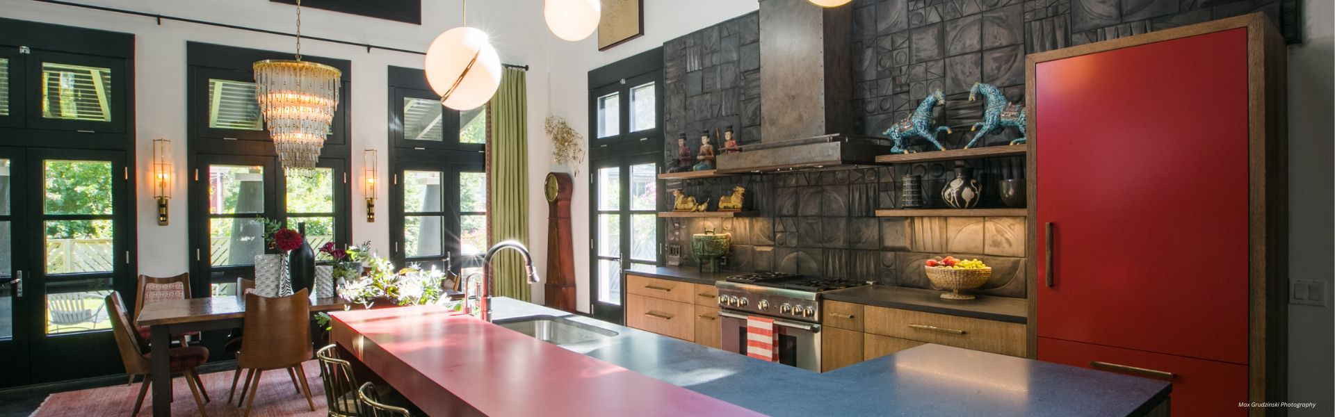 Modern kitchen featuring Banner Boulder Custom ✅-2, black-framed windows, a large red refrigerator, gray countertops, wooden cabinets, open shelves, a chandelier above the dining table, and pendant lights over the island.