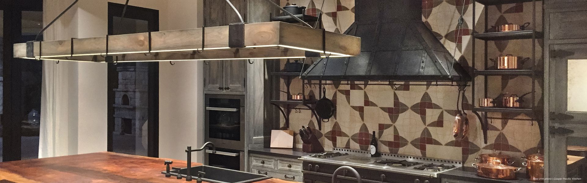 The Banner Breckenridge Custom features a modern rustic kitchen with a large wooden island, industrial-style light fixture, patterned tile backsplash, metal range hood, open shelves with copper cookware, and built-in oven appliances.