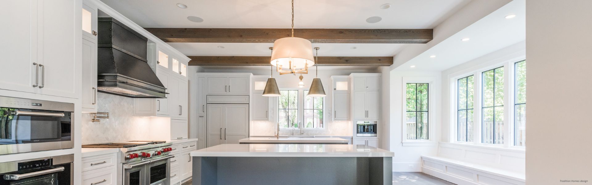 Banner Creede Custom Modern kitchen featuring Banner Creede Custom white cabinets, a large island with a white countertop, built-in appliances, exposed wooden beams, pendant lights, and expansive windows that fill the space with natural light.