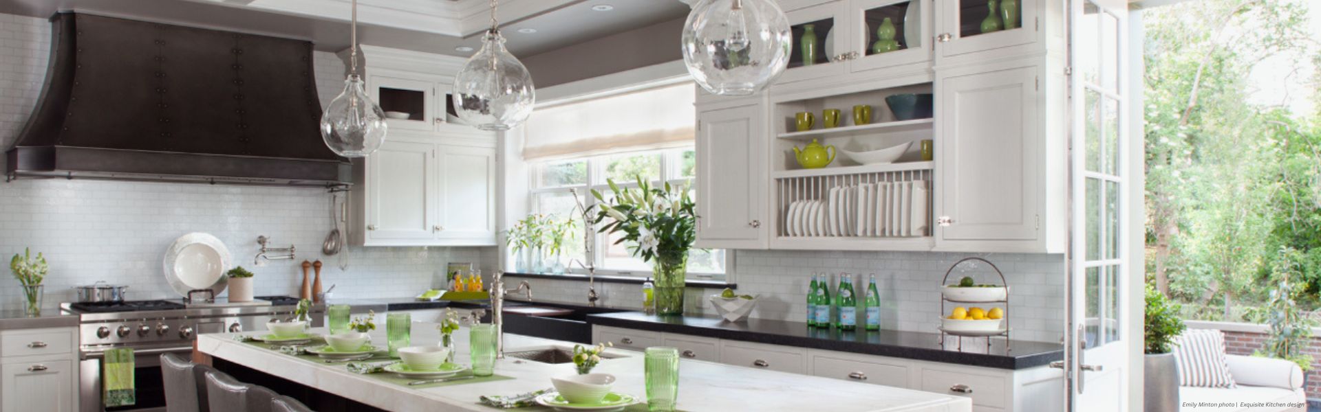 Banner Winter Park Custom Modern kitchen featuring Banner Winter Park Custom white cabinets, dark countertops, a large island with green dishware, pendant lights, stainless steel appliances, open shelves with dishes, and glass doors to the garden.