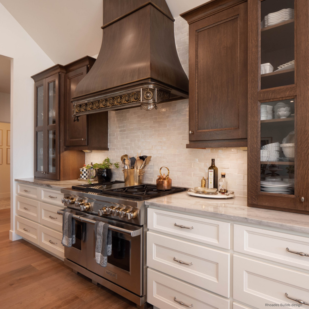 Bellvue gallery1 Bellvue gallery1 features a modern kitchen with dark wood upper cabinets, white lowers, a stainless steel stove, large decorative range hood, marble countertops, light tile backsplash, and open shelves for dishes and cookware.