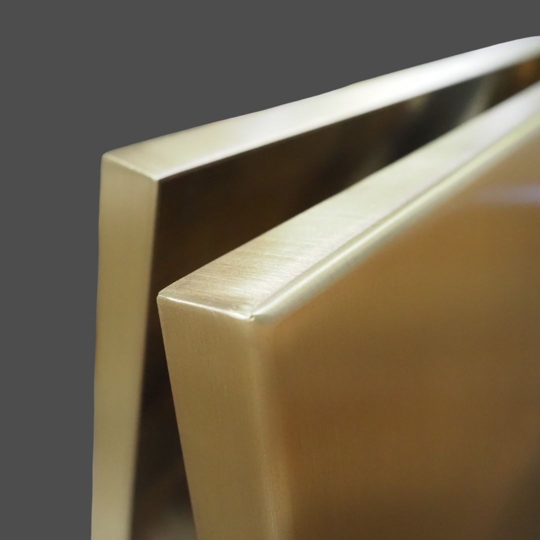 Brass Burnished 2 Brass Burnished 2 features two brushed metal panels with smooth, reflective surfaces and sharp edges, positioned at an angle against a plain gray background.