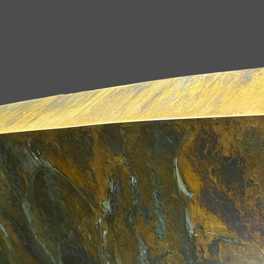 Brass Washed 3-5 Close-up of the edge of Brass Washed 3-5, a dark, textured stone surface featuring brown, gold, and black patterns, set against a plain gray background.
