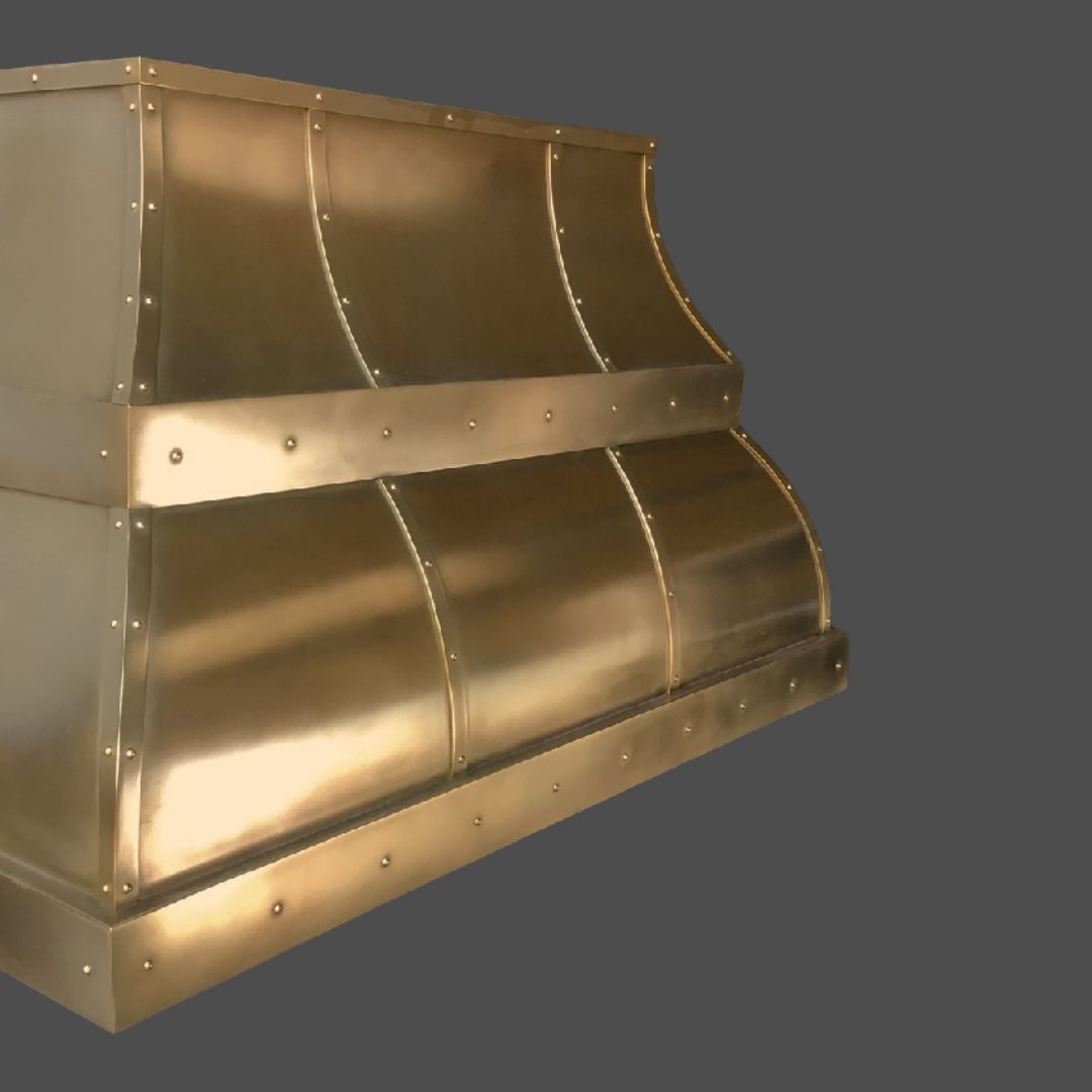 Bronze Burnished 3 The Bronze Burnished 3 kitchen range hood features curved panels and visible rivets in a brass finish, displayed against a plain gray background.