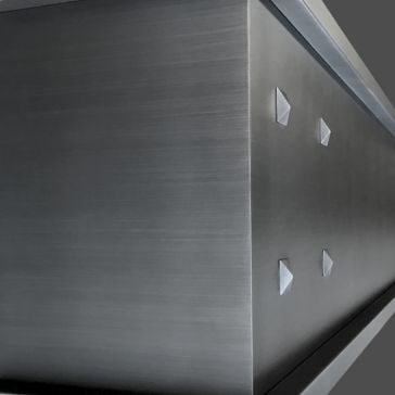 Brushed 2 Close-up of Brushed 2's metallic, brushed steel surface featuring four pyramid-shaped studs in a square on one side. The focus is on the object's smooth, industrial corner.