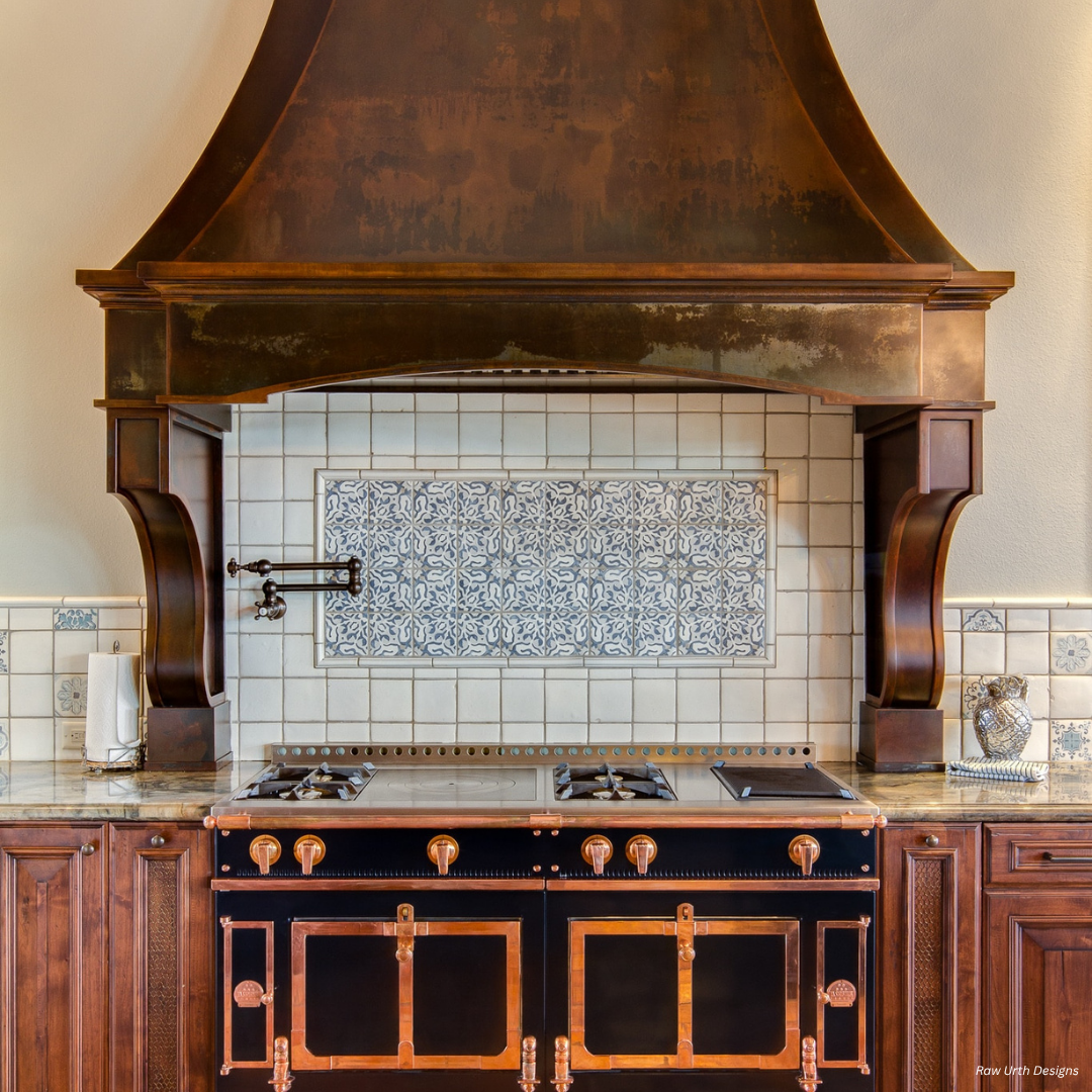 Cherry Hills gallery3 Cherry Hills gallery3 showcases a gourmet kitchen with a black and copper stove, ornate dark range hood, blue and white tile backsplash, wood cabinets, and a paper towel holder to the left.