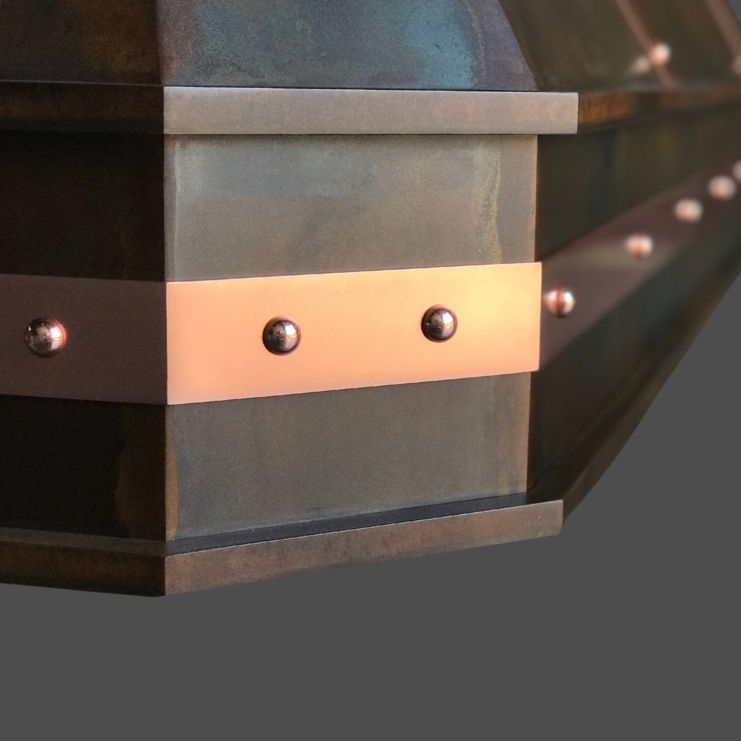 Copper Burnished 3 Close-up of the Copper Burnished 3, a metal object with a bronze band and round rivets, showcasing an angular industrial design against a plain gray background.