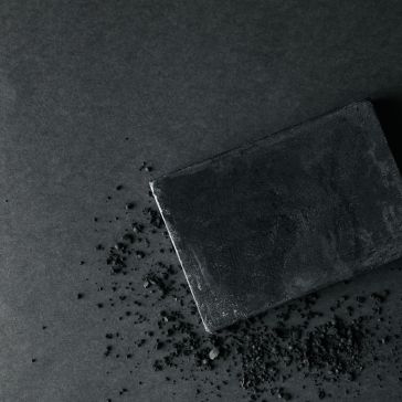 Dark Antique 4 The Dark Antique 4 is a rectangular black bar displayed on a dark surface, accented by scattered black powder, creating a monochromatic and textured visual effect.