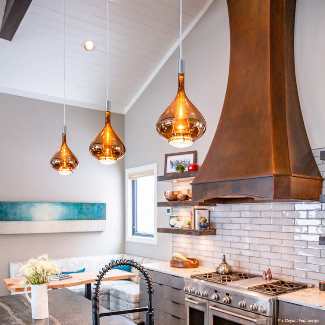 Durango gallery3 A modern kitchen with Durango gallery3 glossy gray subway tiles, a copper range hood, and three amber glass pendants. Built-in shelves display colorful dishes, and a cozy dining nook with flowers sits by the window.