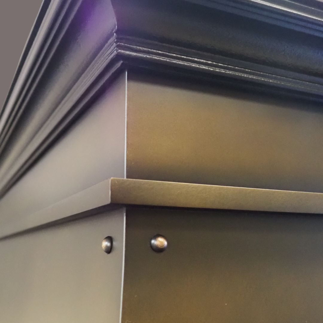 Close-up of the Foundry 2’s corner, showing decorative trim with two round rivets and smooth, dark matte surfaces. Sharp lines and edges highlight its metallic structure.