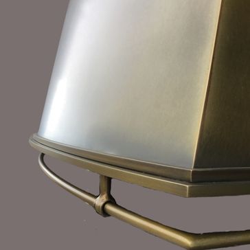 Close-up of the Foundry 2549: a metallic lampshade with a brushed finish, geometric edge, and supporting metal rod underneath, set against a plain grey background.