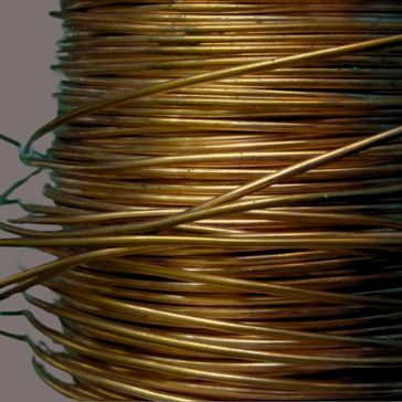 A close-up of Foundry 6720 shows a tangled coil of thin, shiny brass wire with multiple tight loops. Its metallic surface reflects light, highlighting the golden color.