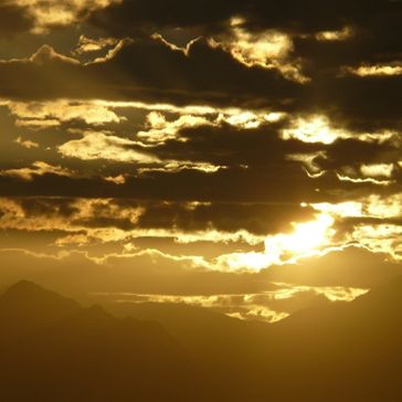 Foundry captures a dramatic golden sunset as dark clouds partially cover the sun, casting a warm glow over distant mountain silhouettes.