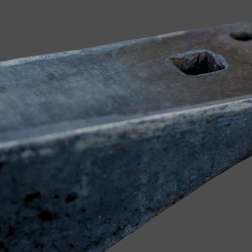 Close-up of Gunmetal 2’s worn metallic surface featuring a hexagonal hole, possibly from an old tool or machine, set against a plain gray background.