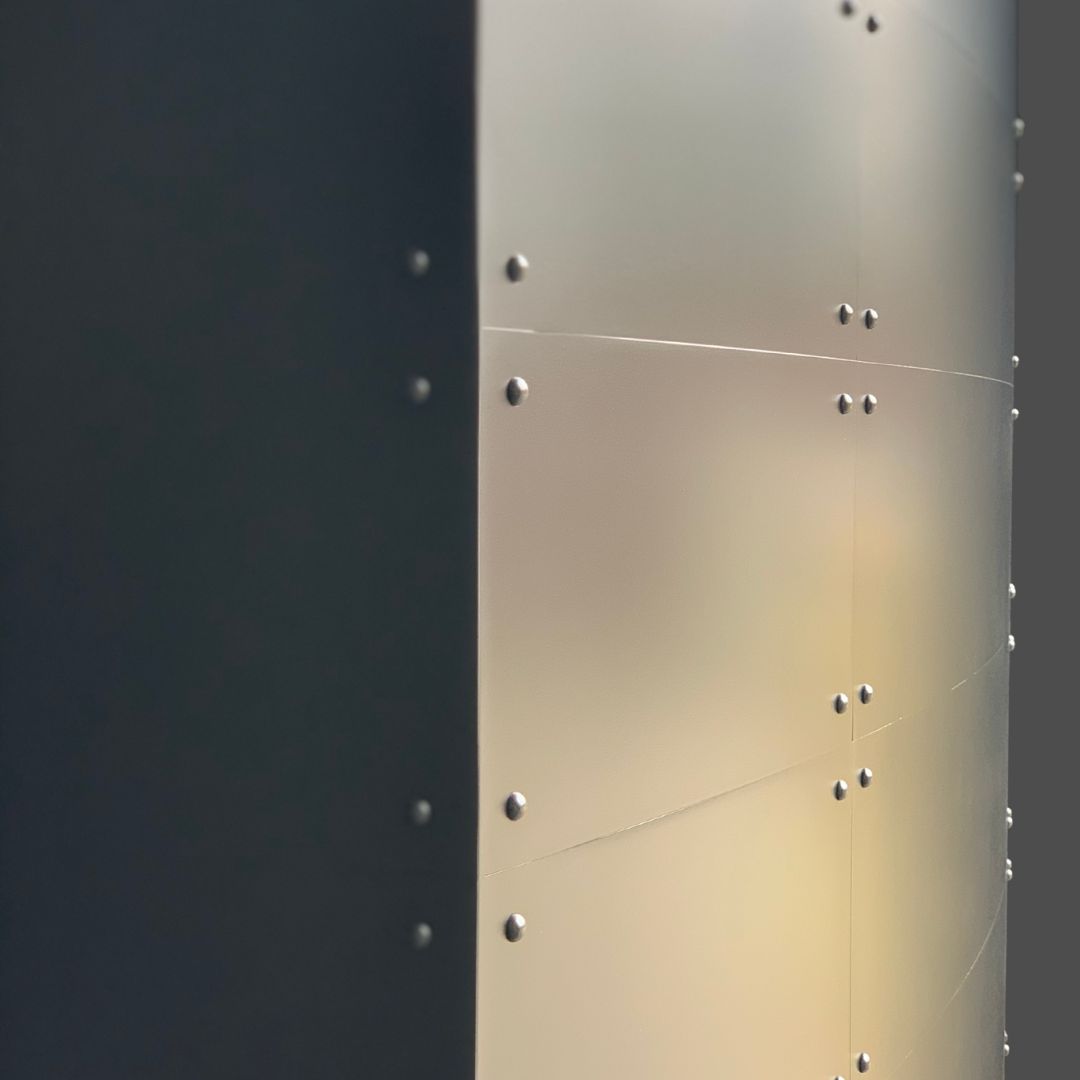 Gunnison gallery3 A close-up of the Gunnison gallery3’s metallic surface features rows of rivets, with one side in shadow and the other brightly lit, creating a dramatic contrast between light and dark.