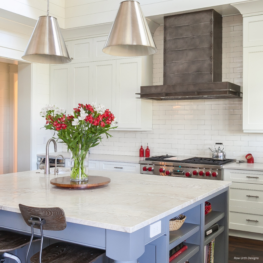 The Leadville gallery1✅ features a modern kitchen with white cabinets, stainless steel appliances, metal pendant lights, a marble island adorned with red and white flowers, and a dark wood range hood above the stove.