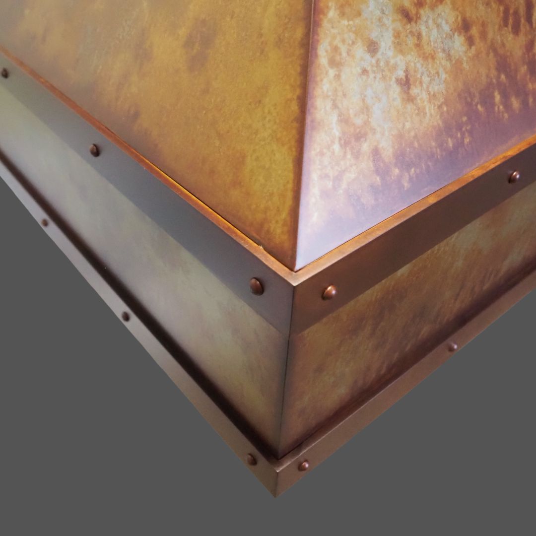 Leathered 1 Close-up of Leathered 1, a metallic, rust-colored, pyramid-shaped object with rivets along the edges, set against a plain gray background.