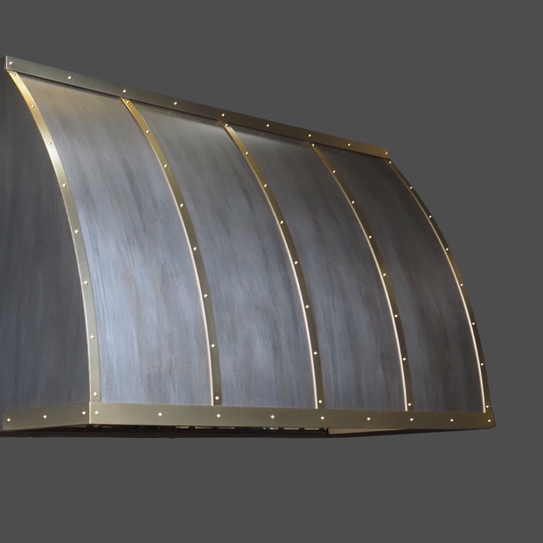 Light Washed 3 The Light Washed 3 is a curved metal range hood featuring a matte gray finish with evenly spaced vertical brass bands and rivets, shown against a plain gray background.