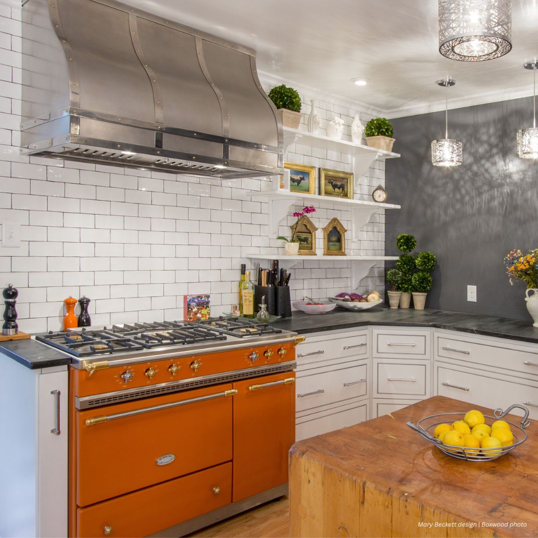 Masonville gallery2 The Masonville gallery2 features a modern kitchen with white subway tiles, an orange vintage-style stove, open shelves with decor and plants, gray countertops, pendant lights, and a wooden island topped with lemons.