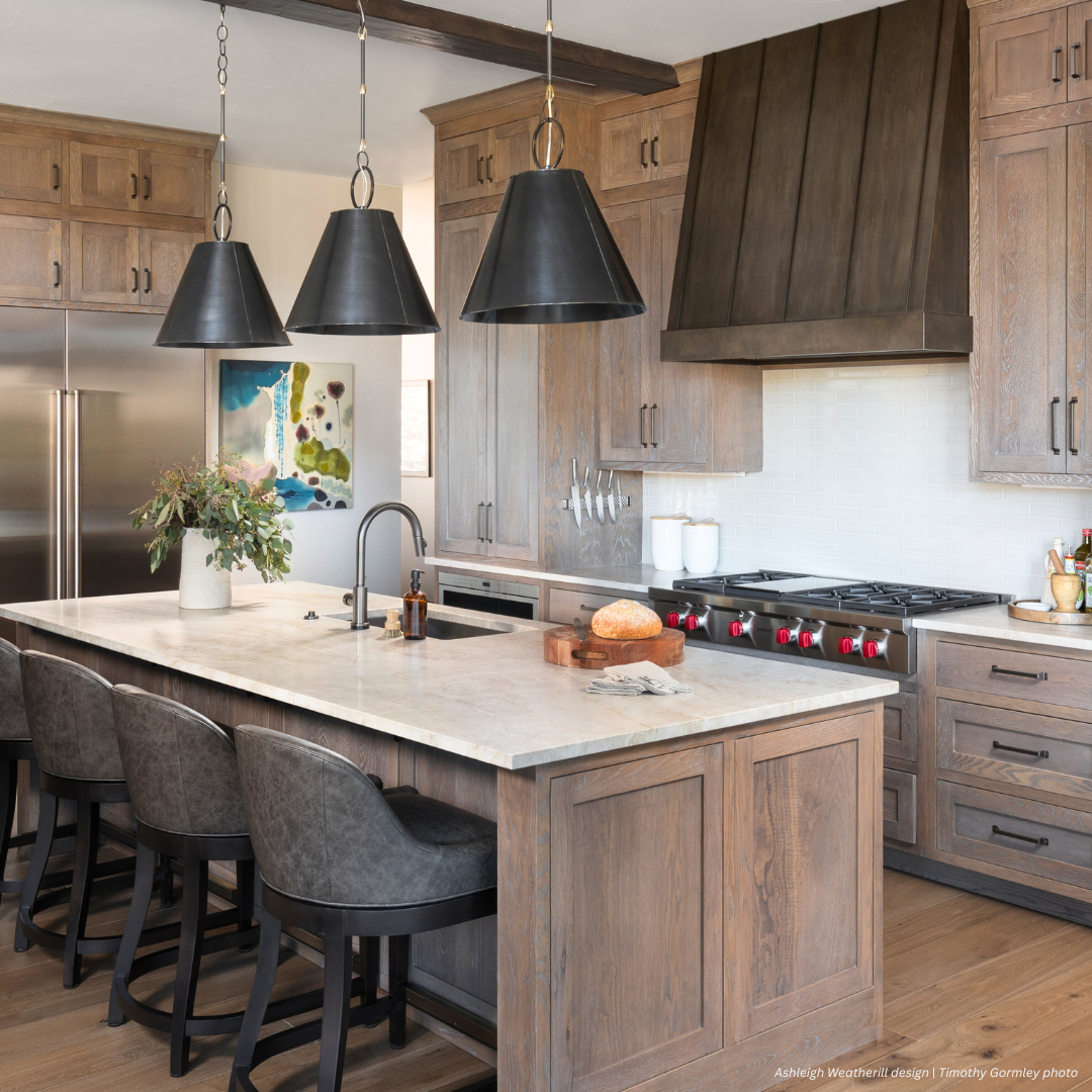 Mesa gallery3✅ Modern kitchen featuring Mesa gallery3 light wood cabinets, large marble island, four dark upholstered bar stools, stainless steel appliances, three black pendant lights, and a colorful abstract painting on the wall.