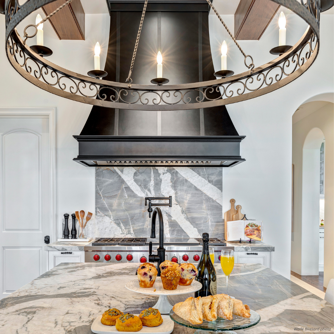 Montrose gallery3 The Montrose gallery3 features a bright, modern kitchen with white walls, a marble island displaying baked goods, orange juice, and wine. A black range hood, chandelier, stove, and marble backsplash complete the stylish space.