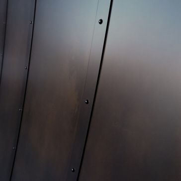 Close-up of Oil Rubbed 2: several dark metal panels with visible seams and round rivets, arranged vertically with a slight curve.